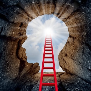 Concept of open mind as a a deep mountain cliff shaped as a human head with a ladder leading to the outside towards a glowing sun as a psychology and mental health metaphor for spiritual discovery.
