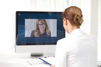 Rear view shot of middle age businesswoman sitting at her workplace and having video chat with executive professional woman.