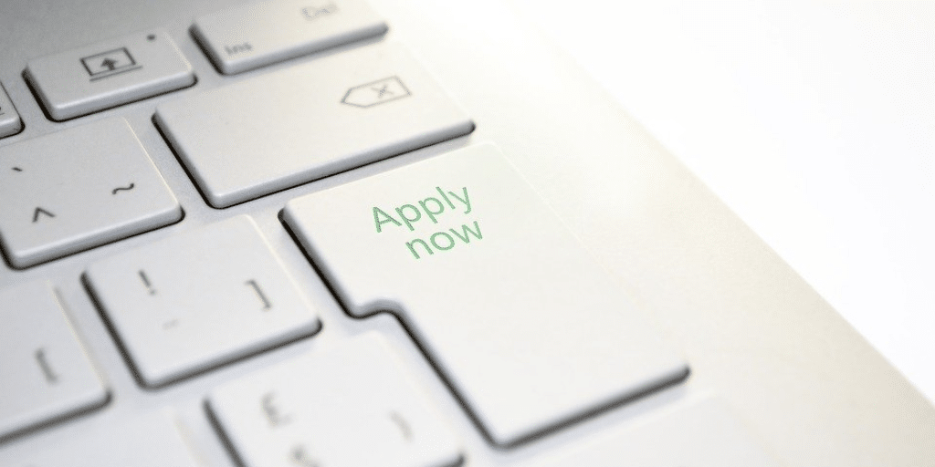 A keyboard with the words "apply now" written on the enter key