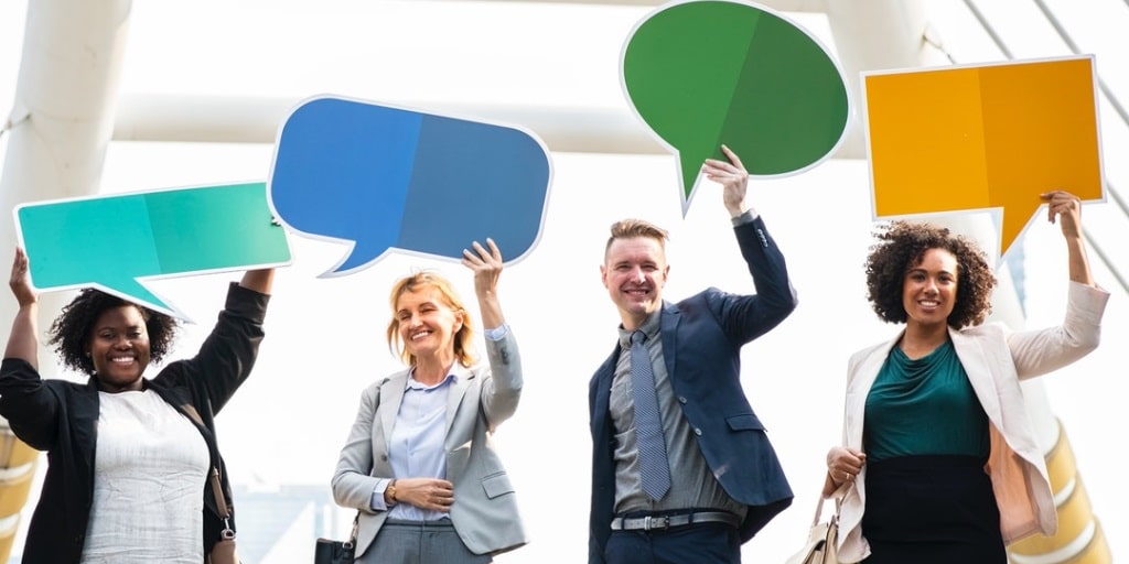 Four business people holding cut-out communication bubbles above their heads.