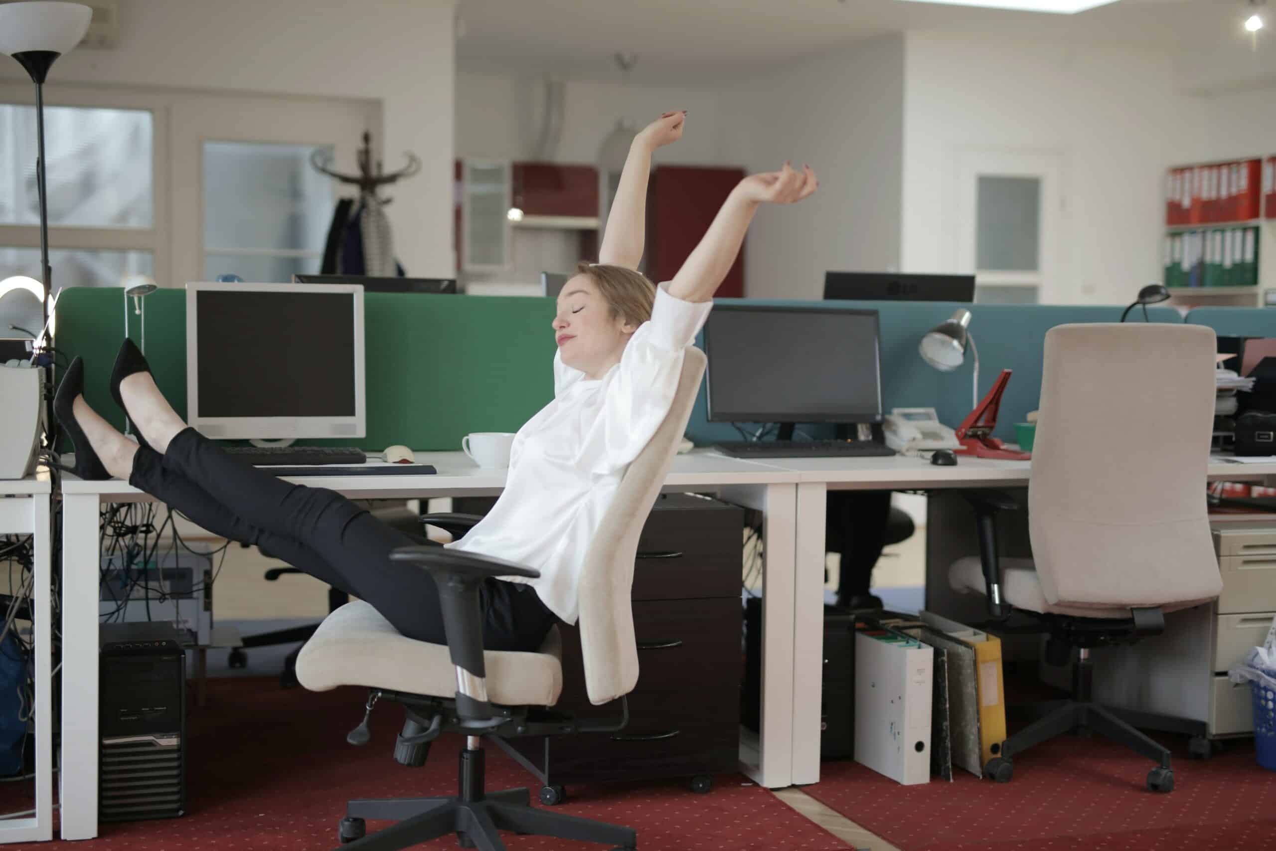a worker with their feet on their work desk and arms raised, meant to signify lounging at work