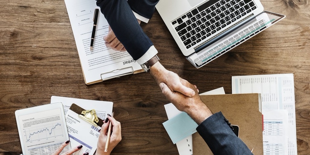 Two business people, on opposite sides of a desk, shaking hands