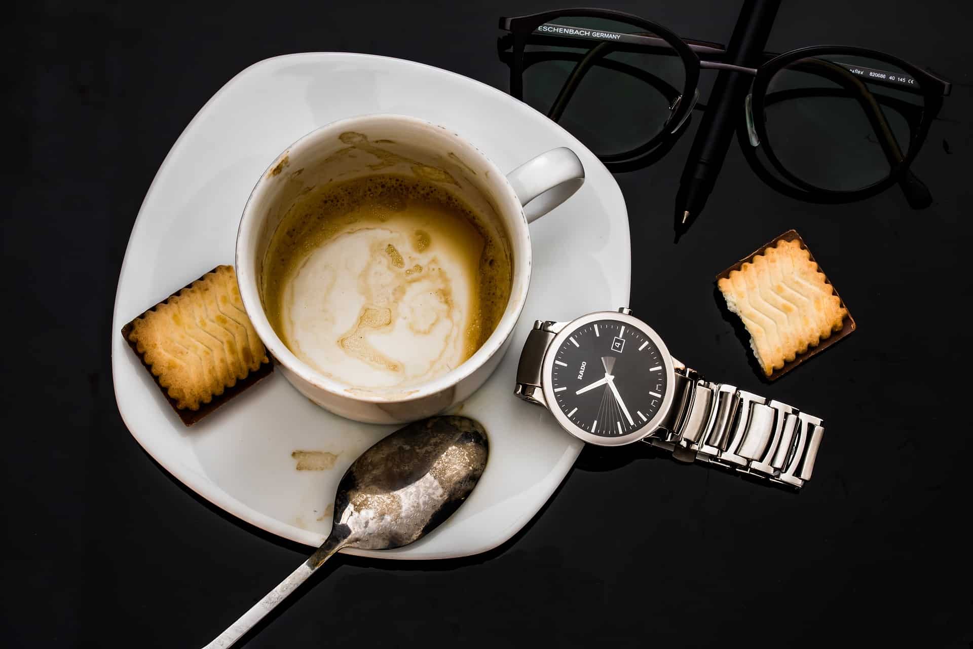 An empty coffee cup on a table along with a watch and glasses