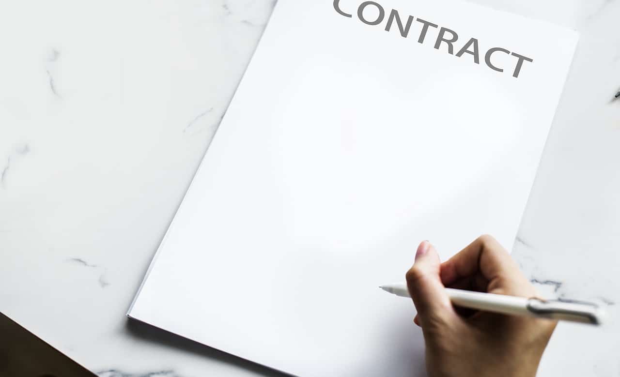 A hand holding a pen about to sign a paper with the word Contract written across the top.